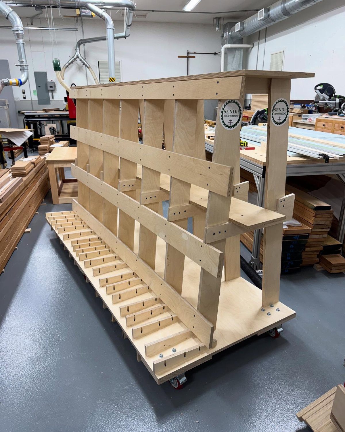 A large wooden mobile lumber rack with multiple shelves on wheels in a workshop.