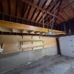 Wooden storage loft and wall-mounted shelves installed in a garage with concrete walls.