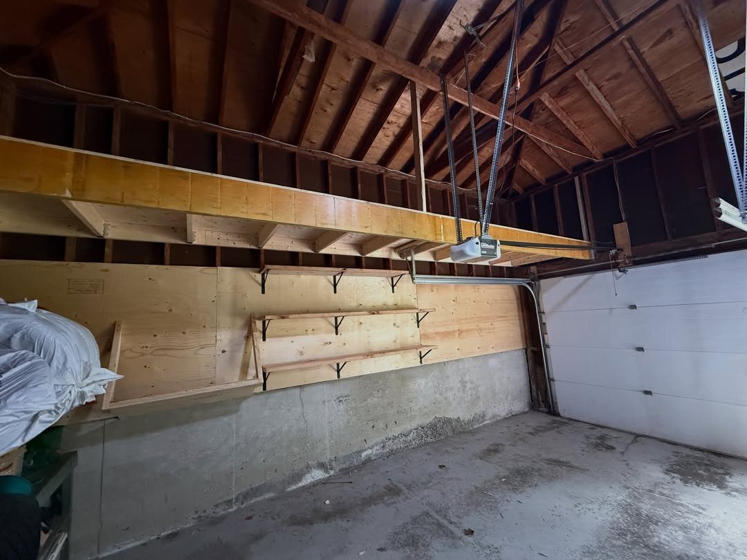Wooden storage loft and wall-mounted shelves installed in a garage with concrete walls.