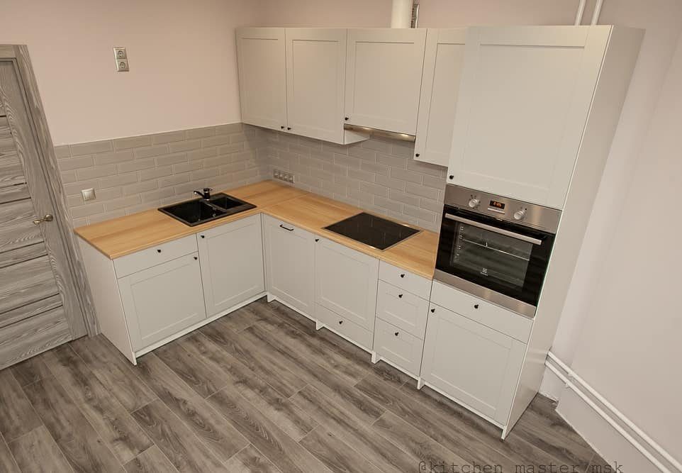 White L-shaped kitchen cabinets with light wood countertops and a built-in oven.