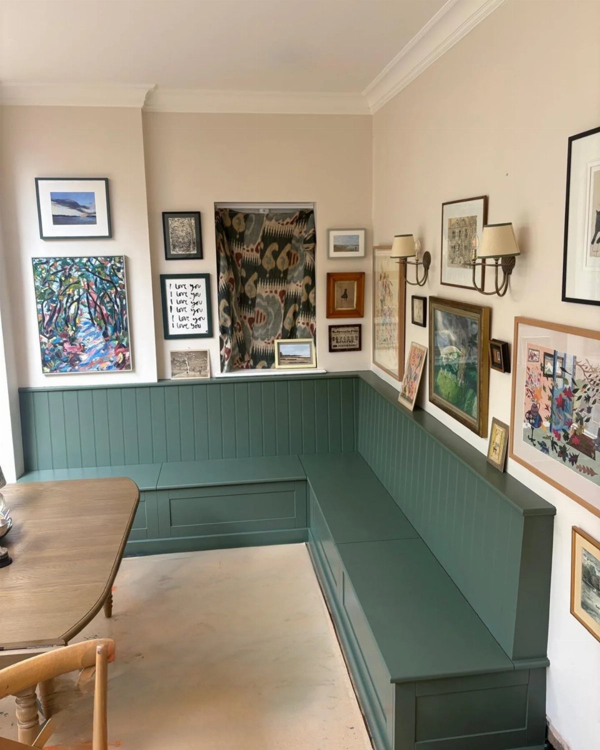 Green L-shaped wooden kitchen banquette with storage drawers against a wall of framed art.