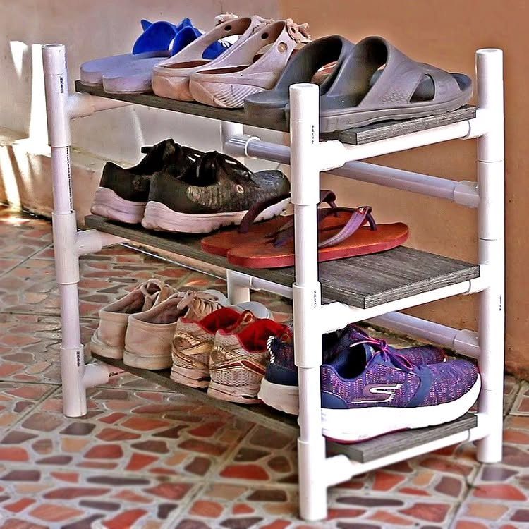 A three-tier shoe rack made of white PVC pipes and wooden planks holding various footwear.