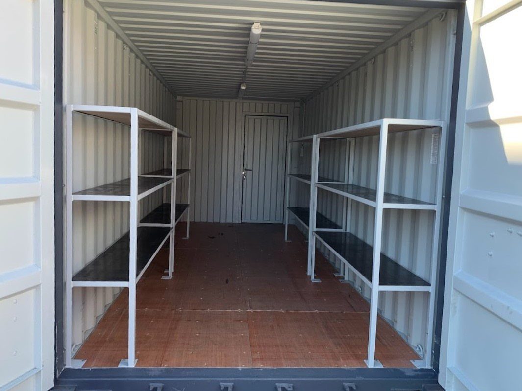 White metal heavy-duty shelving units installed inside a large white shipping container.