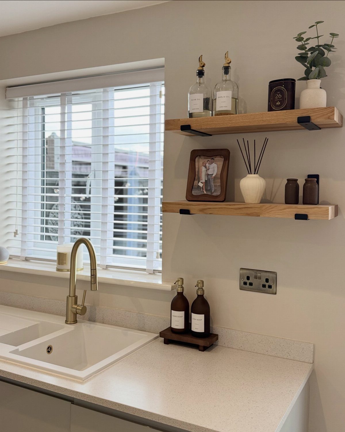 A gold single-handle kitchen faucet installed on a white sink by a window with blinds.