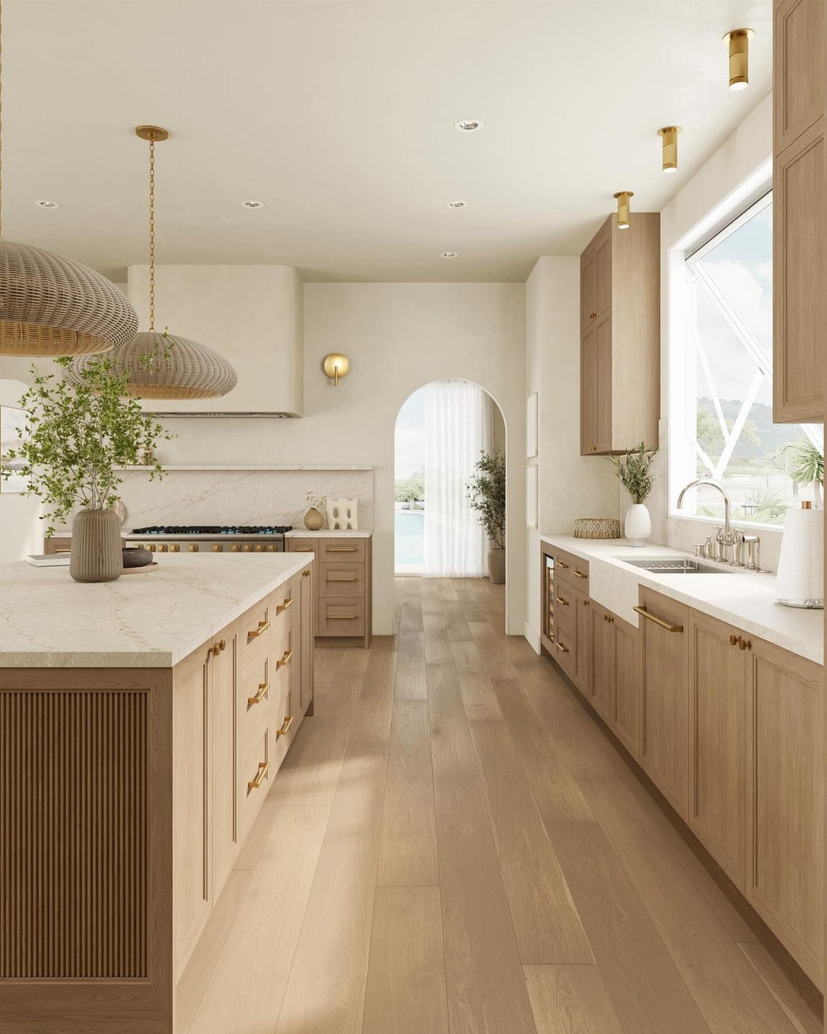 A bright modern kitchen with light wood cabinets, marble countertops, and gold pendant lights.